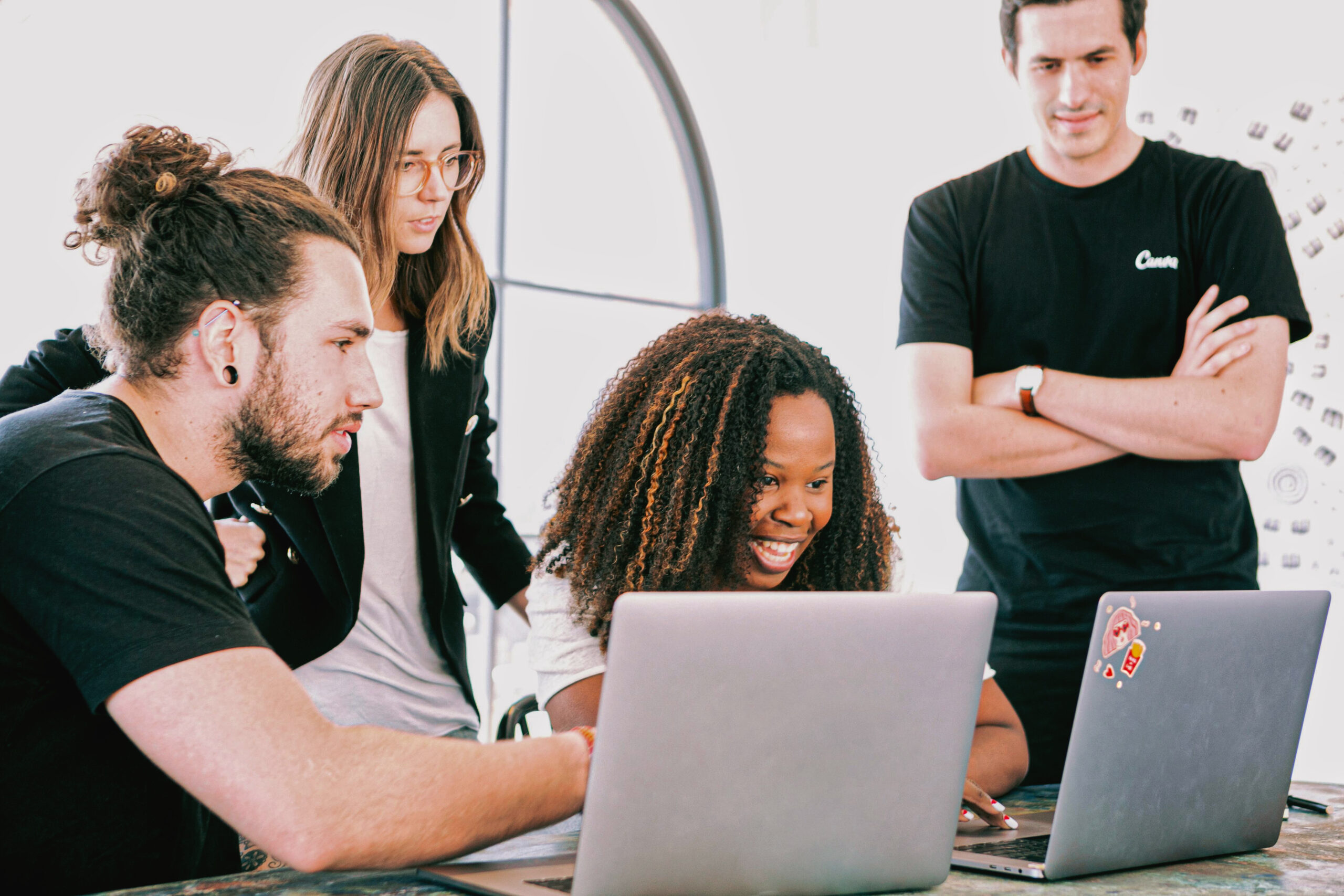 a diverse group of young hip people dressed in black and white huddle around a couple of laptops